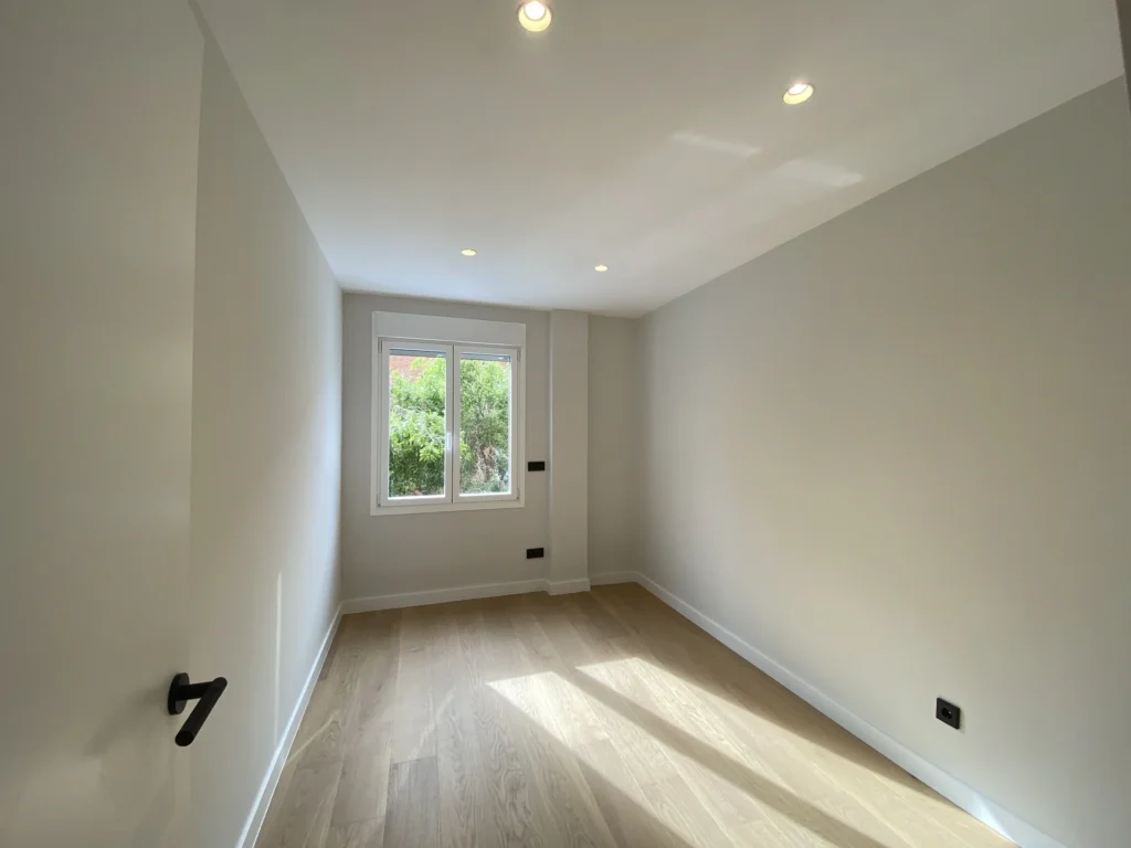 Habitación reformada con suelo de madera y paredes lisas en proyecto de reforma integral en Madrid por Mokara Estudio.