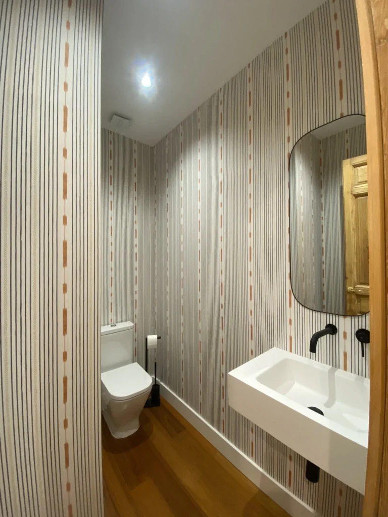 Baño moderno con papel tapiz rayado gris y lavabo flotante en Barrio de Justicia, interiorismo elegante