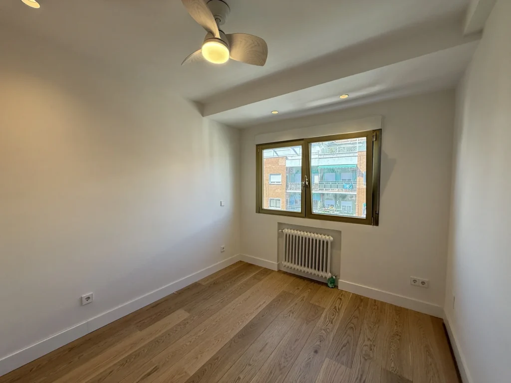 Dormitorio reformado en la capital con ventana luminosa, radiador y suelo madera, diseño interior moderno
