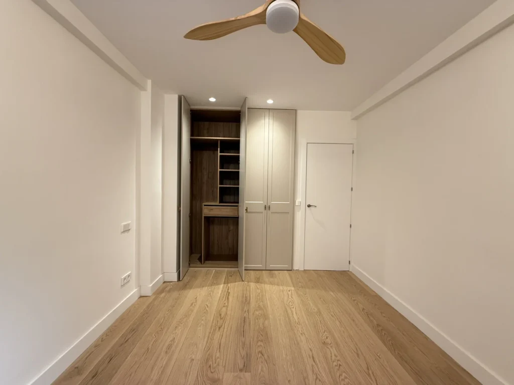 Dormitorio luminoso con ventilador de madera en techo y armario entreabierto en reforma de interiorismo cerca de la Gran Vía de Bravo Murillo, estilo escandinavo moderno.