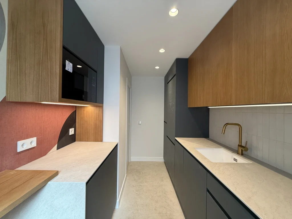 Cocina reformada cerca de la Gran Vía de Bravo Murillo: armarios altos en madera y gris, suelo claro y electrodomésticos empotrados.